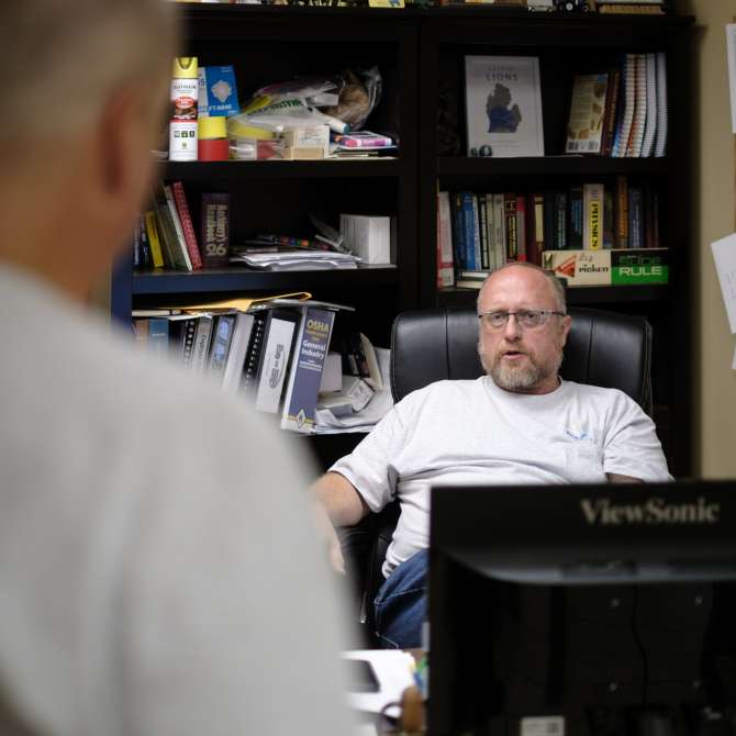 Man sitting relaxed at desk while someone is talking with him