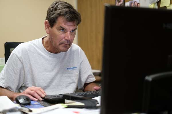 man in white shirt focused on typing at computer